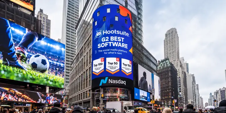 Auf einer Werbetafel am Times Square ist die Auszeichnung „G2 Best Software“ von Hootsuite zu sehen, daneben auf einem Bildschirm Fußballbilder und darunter Auszeichnungsabzeichen.